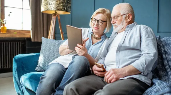 elderly couple sat on sofa looking at tablet device together