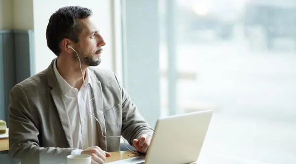 Man sat at laptop with headphones on looking out window