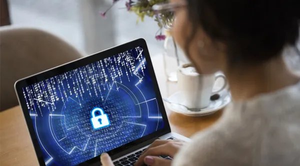 Kvinna med glasögon tittar på en laptopskärm med en cybersecurity symbol i form av ett hänglås