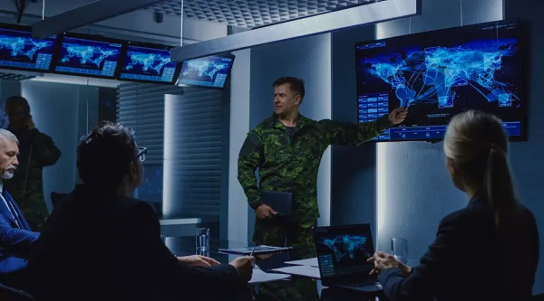 People discuss a map displayed on a screen in a mission control room