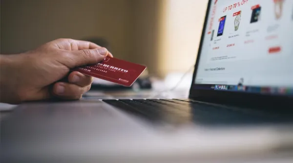 En hand som håller i ett betalkort framför en laptop där skärmen visar en online shoppingsida