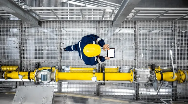 Refinery worker with yellow hardhat walking by gas pipes