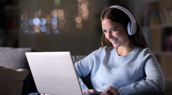 A smiling person wearing headphones looking at a laptop