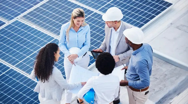 Group of sustainability consultants, some with hard hats, meeting outside near solar panels