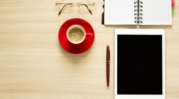 tablette, café, lunettes et cahier de note sur un bureau
