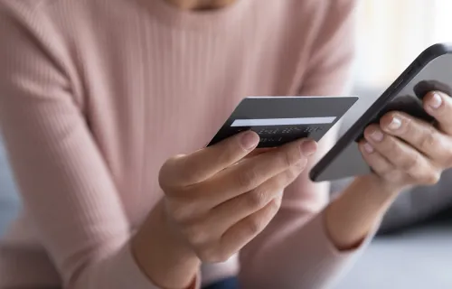 Person holder bankkort og mobiltelefon for digital betaling.