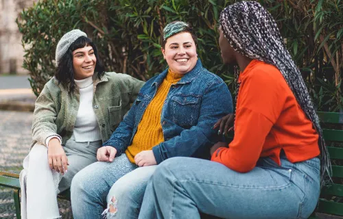 three people talking outside and laughing on a bench
