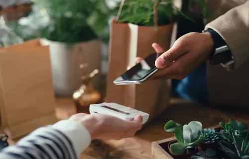 Kunde betaler kontaktløst med mobiltelefon ved betalingsterminal.