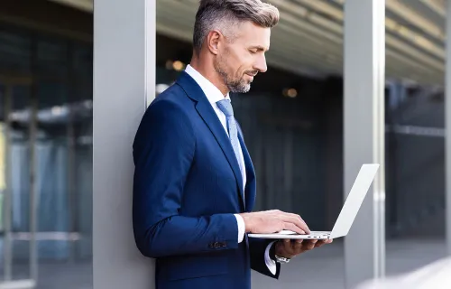 Business Man steht mit seinem Laptop in der Hand vor einem Bürogebäude
