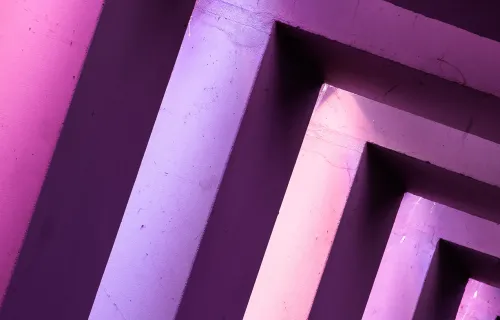 Abstrakt bild av geometriska arkitektoniska former i en diagonal komposition, upplysta med lila och rosa ljus. Bilden skapar en illusion av djup och perspektiv.