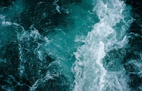 Närbild av havsvatten där vågor och skum bildar ett abstrakt mönster i turkosa och mörkgröna…