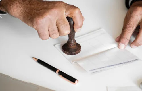 Närbild på två händer som håller i en stämpel och bankdokument, på bordet ligger också en penna