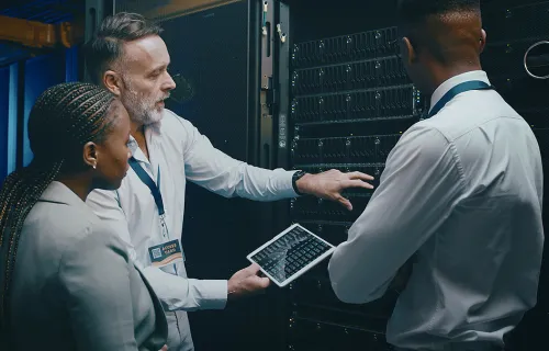 Three cybersecurity professionals using a tablet in a server room