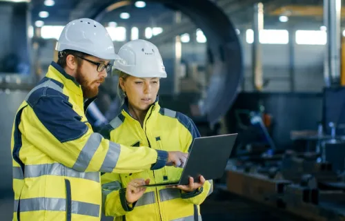Deux personnes portant un casque et un gilet réflechissant consultent une tablette