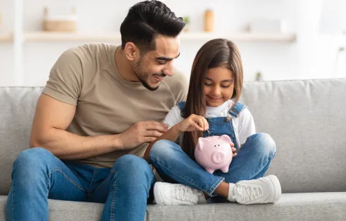 Father and daughter putting money into a piggy bank