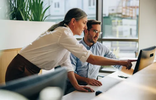 Deux professionnels collaborent devant un ordinateur dans un environnement de bureau.
