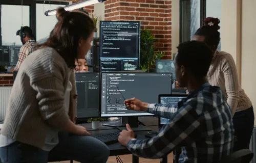 developers gathered round a desktop with code on the monitor