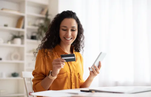 Junge Frau will einen Bezahlvorgang via Iphone vornehmen und schaut dabei auf ihre Kreditkarte