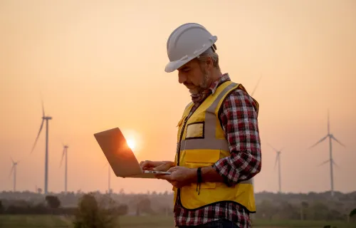 A man wearing a high-visibility jacket and a hard hat using a laptop