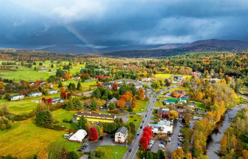 Aerial view of a rural town with autumn foliage and storm clouds over mountains