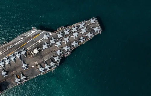 Aerial view of an aircraft carrier with multiple fighter jets lined up on the front