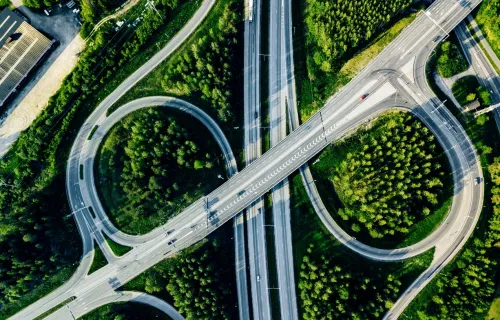 Luftaufnahme eines Autobahnkreuzes mit mehreren Überführungen, umgeben von grünen Waldflächen.