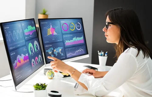 En kvinnlig analytiker som tittar på KPI:er från sitt affärssystem på två skärmar