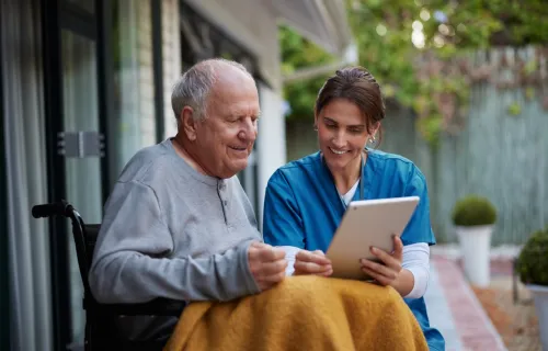 Care worker sitting with elderly patient looking at Ipad 