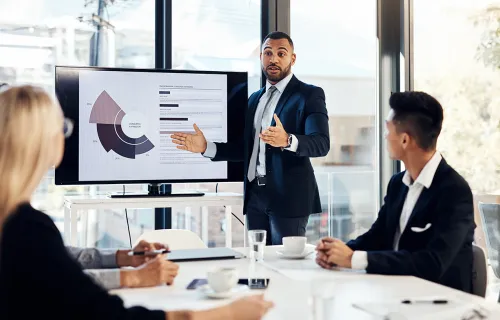 A business man presenting to two colleagues on a large monitor
