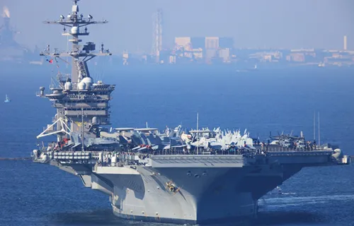 Aircraft carrier on calm blue waters with a cityscape in the background
