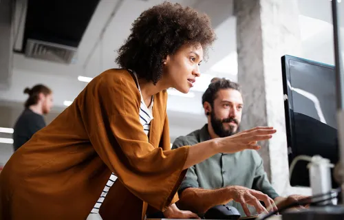 Två kollegor står och diskuterar något vi en datorskärm