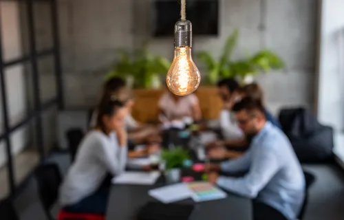 team of people sitting around conference table under glowing light bulb