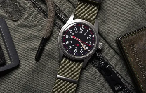 Ett armbandsur med militärgrönt klockband ligger på en militärgrön väska
