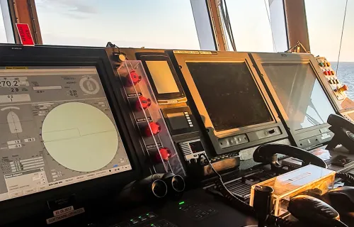Dashboard on the bridge of a boat, loads of screens, two black telephones and buttons for navigation system
