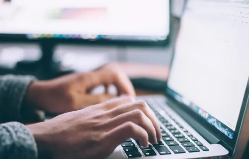 Två händer syns i närbild där de skriver på ett tangentbord på en laptop