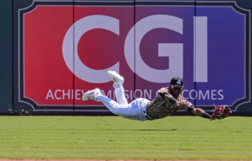 CGI logo in the outfield of the Trash Panda stadium in back of a baseball player diving for a…