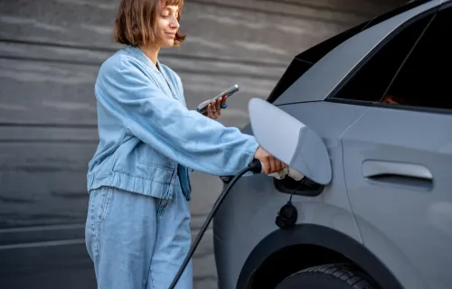 Woman checks her phone while charging an electric car