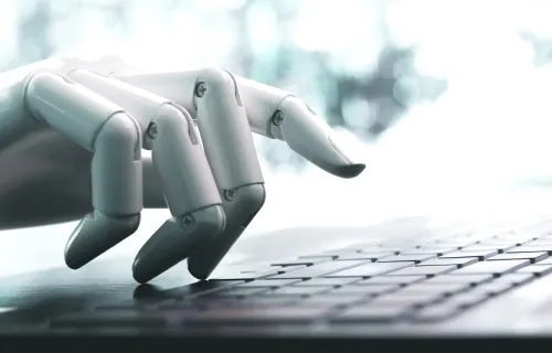 robot hand representing chatbots and intelligent automation typing on a laptop
