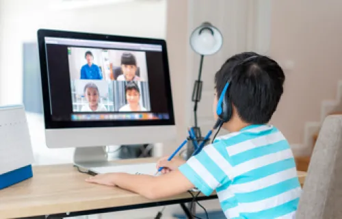 Ein Kind sitzt vor dem PC und verfolgt den Online-Unterricht mit seinen Klassenkameraden