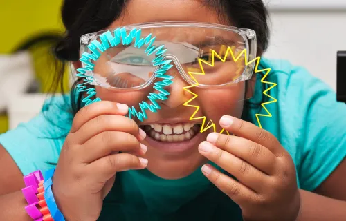 Child wearing safety googles smiles with paper shapes