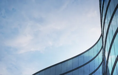 Curved glass facade of a modern building reflecting a cloudy blue sky