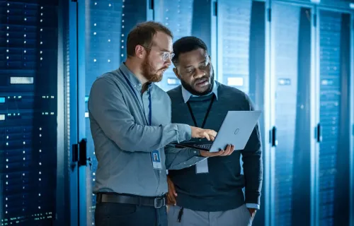 two data professionals review information on a laptop in a data center
