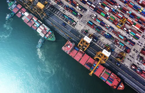 Flygfoto över en containerhamn med lastfartyg, kranar och färgglada containrar staplade längs…