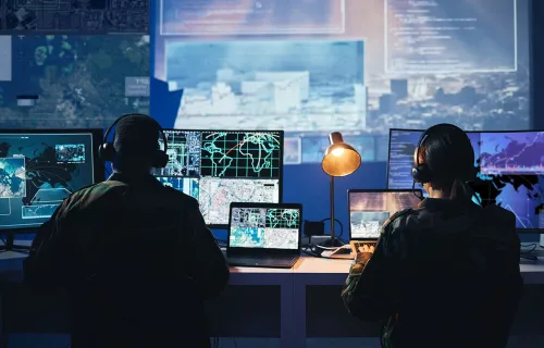 Två personer sitter framför flera datorskärmar i ett övervaknings- eller säkerhetscenter…