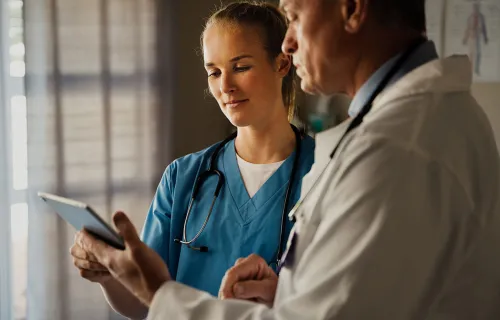 Två läkare, en i blå sjukvårdskläder och en i vit rock, granskar information på en surfplatta…