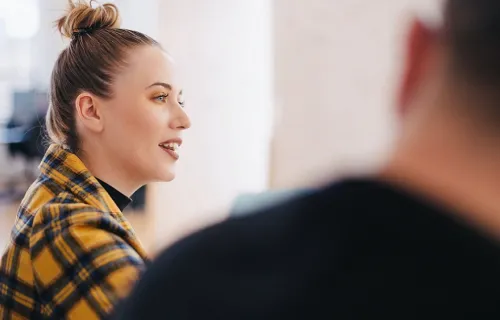 Kvinna sitter och pratar med en kollega vars ryggtavla som syns i förgrunden