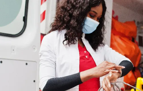 Sanitäterin mit Maske vor einem Rettungswagen 