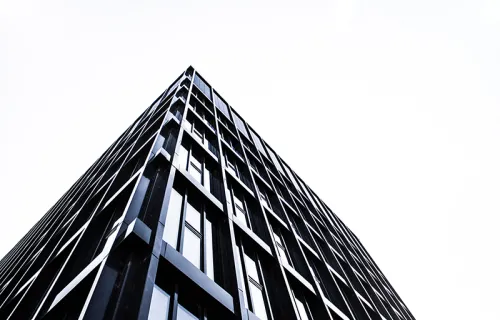 Ett höghus i glas och stål ses nedifrån när det tornar upp sig mot en vit himmel