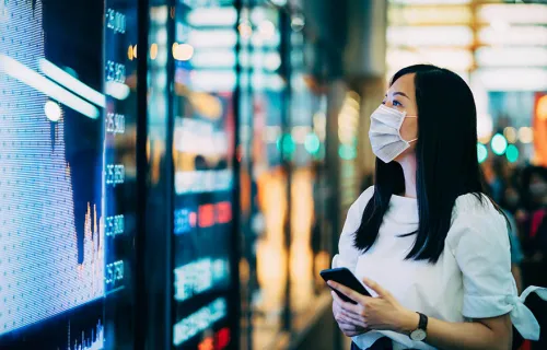 woman in a medical facemask looking at figures ona digital display board