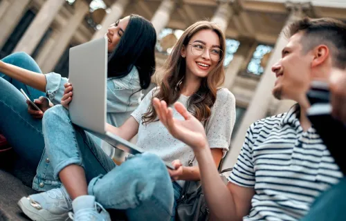 Group of students chat happily around a laptop